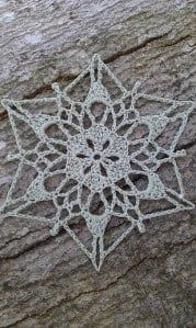 a white crocheted snowflake sitting on top of a rock