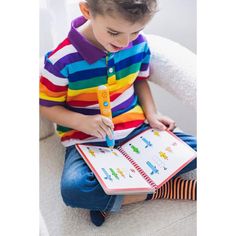 a young boy sitting on a chair holding a book and pen in his hands while looking at it