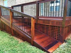 a wooden deck with trellis and railings in the grass next to a brick building