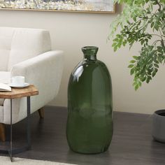 a large green vase sitting on top of a wooden floor next to a white couch