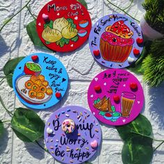 four magnets with different designs on them sitting next to some plants and flowers in front of a white brick wall