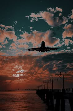 an airplane is flying over the water at sunset