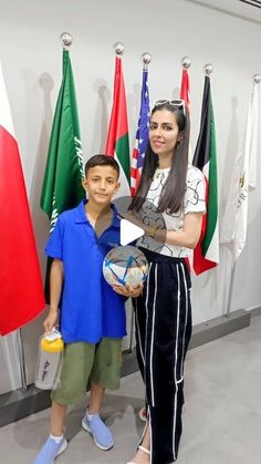 a woman holding a soccer ball and standing next to a boy in front of flags