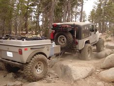 an off - road vehicle driving on rocks in the woods with another jeep behind it