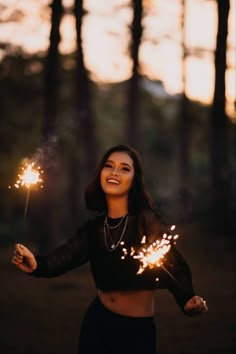 a woman holding sparklers in her hands and smiling at the camera with trees behind her