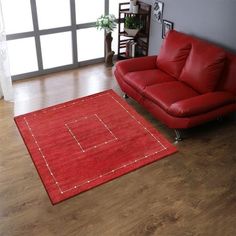 a living room with a red leather couch and rug on the wooden floor next to a window