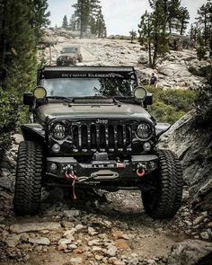 a jeep driving down a rocky trail in the woods with its lights on and off