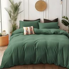 a bed with green sheets and pillows in a room next to a potted plant