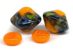 three orange and black glass beads with leaves on them, sitting next to each other