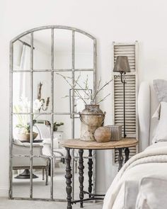 a mirror sitting on top of a bed next to a table with flowers in it