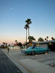 a blue car parked on the side of a road next to palm trees and a house