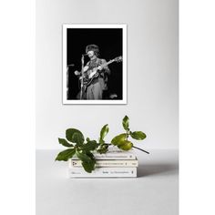 a black and white photo of a man playing the guitar in front of a stack of books