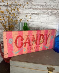 a wooden sign that says candy shop sitting on top of an old trunk next to some vases