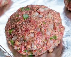 a hamburger covered in meat and vegetables on aluminum foil