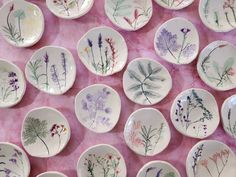 many plates with flowers painted on them sitting on a pink tableclothed surface in front of each other