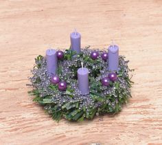 purple candles are placed in a wreath with greenery and beads on the table top