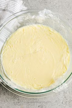 a glass bowl filled with yellow batter on top of a gray counter next to a white towel