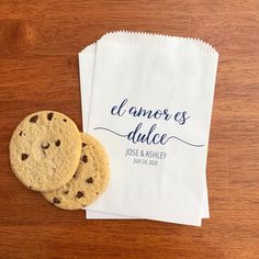 two chocolate chip cookies sitting on top of a white paper bag next to a brown wooden table