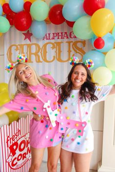 two young women standing next to each other in front of a circus sign and balloons