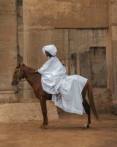 a man in white riding on the back of a brown horse next to a building