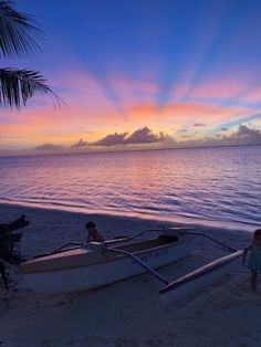 two small boats sitting on top of a sandy beach next to the ocean at sunset