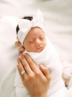 a woman holding a newborn baby wrapped in a white wrap and wearing a diamond ring