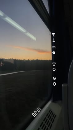 the sun is setting over an open field from inside a train window, with trees in the distance