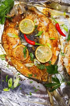 two fish on tin foil with lemons, peppers and green herbs next to them