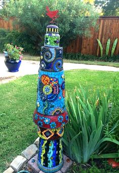 a tall colorful sculpture sitting in the middle of a yard next to a flower pot