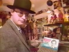 a man wearing a hat and glasses holding a cd in front of a record player