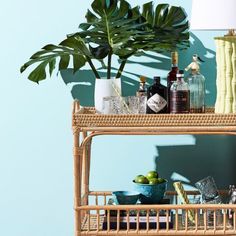 a wicker bar cart with bottles and glasses on it next to a potted plant