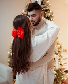 a man and woman standing in front of a christmas tree with a red bow on their hair