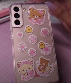 a phone case with stickers on it sitting on a pink surface next to a keyboard