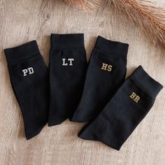 three pairs of black socks with gold letters on them sitting on a wooden floor next to wheat