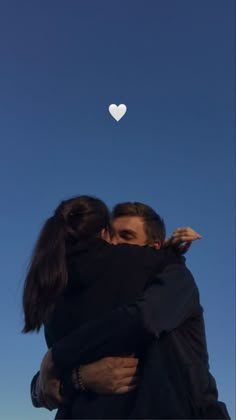 two people hugging each other with a heart shaped object in the sky behind them on a sunny day