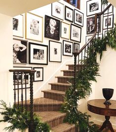 a staircase decorated with christmas greenery and framed pictures on the wall above it, along with potted plants