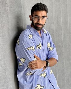 a man wearing glasses leaning against a wall with his arms crossed and looking at the camera