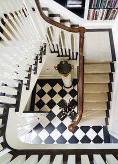 an overhead view of a staircase with black and white tiles on the floor, bookshelf in the background