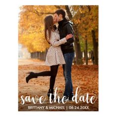 save the date photo magnet with an image of two people kissing in front of fall leaves