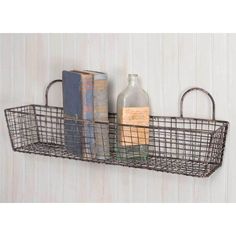 a metal basket with books and a bottle on top is hanging from the wall next to a book shelf