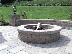 a fire pit sitting on top of a brick patio next to a lush green field