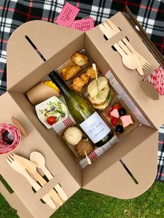 an open cardboard box with food and utensils in it sitting on the grass