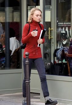 a woman standing on a street corner holding a piece of paper and looking at her phone