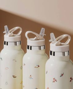 three white water bottles sitting on top of a wooden table next to each other with designs on them