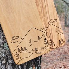 a wooden board that is on top of a tree in the woods with mountains drawn on it