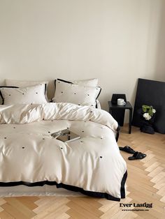 a bed with white sheets and black trim in a room next to a lamp on a wooden floor