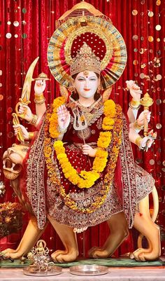 a statue of the hindu god ganesha in front of a red curtain with gold and white decorations