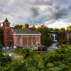 an old red brick building with a waterfall in the back ground and trees around it