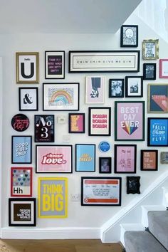 a wall with many framed pictures on it and stairs leading up to the second floor