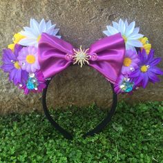 a purple minnie mouse ears headband with flowers and pearls on the side, sitting in grass